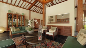 A spacious living room with a high ceiling, wooden beams, a green sofa, a round table, and a bookshelf filled with books. - Villa Desa Roro Dua by Villa Finder (Canggu)