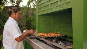A person grilling skewers on a charcoal grill outdoors. - Villa Desa Roro Dua by Villa Finder (Canggu)