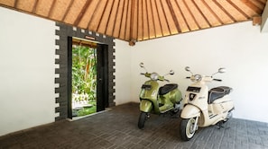 A covered area with two scooters parked, a door labeled 'DESA RORO,' and a view of greenery outside. - Villa Desa Roro Dua by Villa Finder (Canggu)