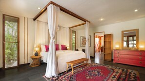 A four-poster canopy bed with a bench, a red dresser, and a patterned rug in a hotel room. - Villa Desa Roro Dua by Villa Finder (Canggu)
