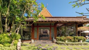A traditional thatched-roof pavilion with a wooden frame, surrounded by lush greenery and a stone pathway leading to the entrance. - Villa Desa Roro by Villa Finder (Canggu)