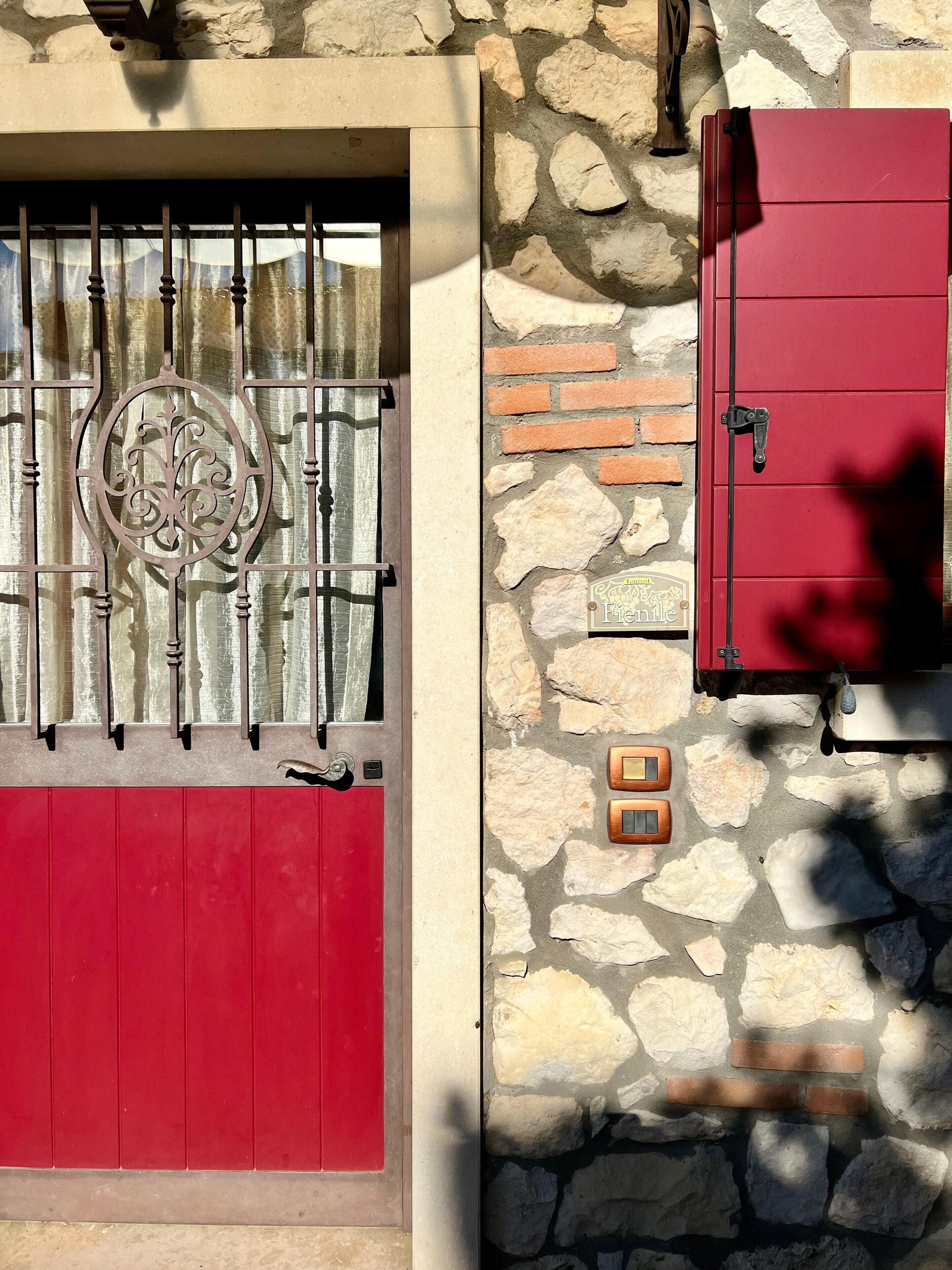 Une porte rouge avec un portail en métal, un mur de pierre avec un motif en briques et un meuble rouge doté d’une poignée.