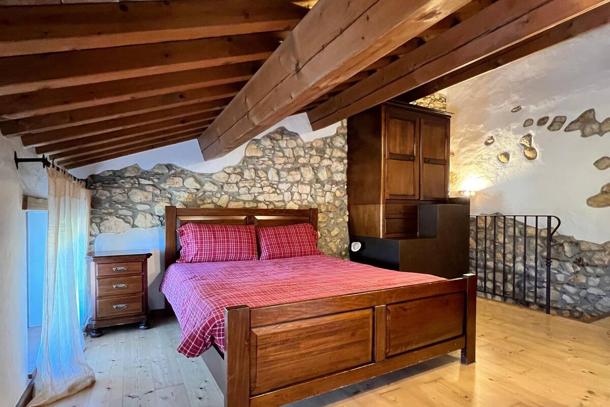 A bedroom with a wooden bed, stone wall, and a stone staircase.