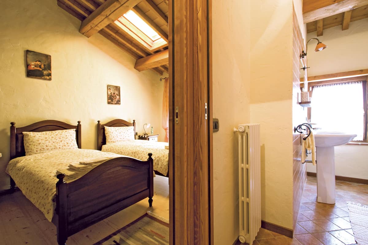 A bedroom with two wooden beds, a radiator, and a bathroom with a sink and window.