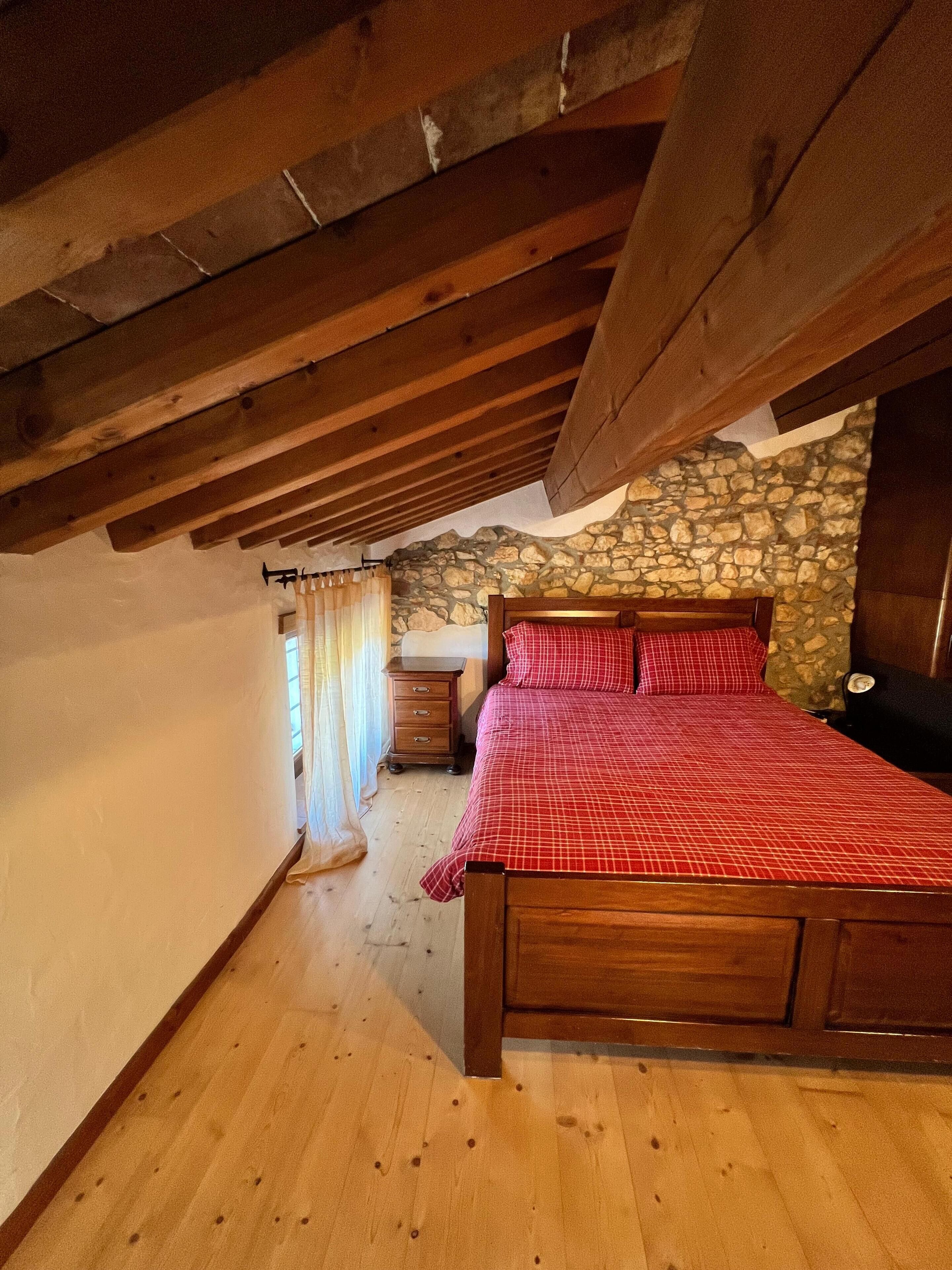 A bedroom with a wooden bed, stone wall, and a wooden ceiling.