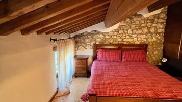 A bedroom with a wooden bed, stone wall, and a wooden ceiling.
