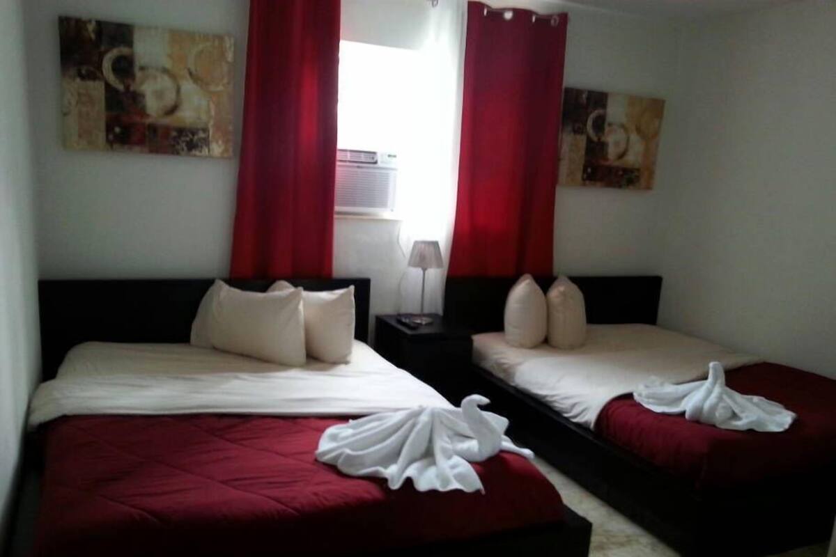 A hotel room with two beds, red curtains, and artwork on the walls.