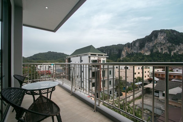 Un balcon avec une table et des chaises, donnant sur un paysage montagneux et une zone résidentielle.
