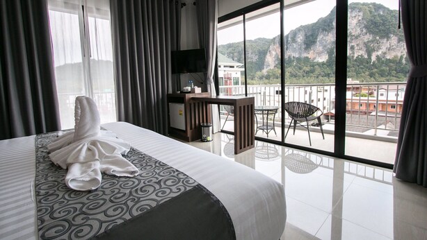 Habitación de hotel con cama, escritorio y balcón con vistas a montañas.