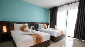 Habitación de hotel con dos camas, una pared verde azulado y un ventanal con cortinas.