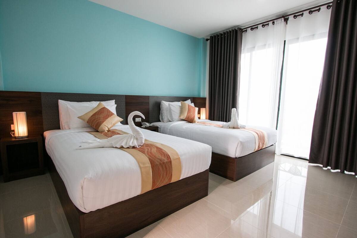 A hotel room with two beds, a teal wall, and a large window with curtains.