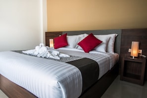 Un lit bien fait, avec une literie blanche et grise, deux oreillers rouges et un ensemble de serviettes blanches posées sur le lit.