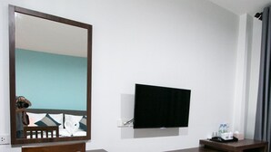Una habitación de hotel con un escritorio de madera, un televisor montado en la pared, un refrigerador pequeño y un cesto de basura.