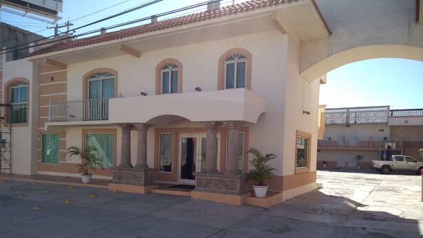 A two-story building with a balcony, a front door, and potted plants. - Hotel Santander Inn & Suites (Ciudad Victoria)