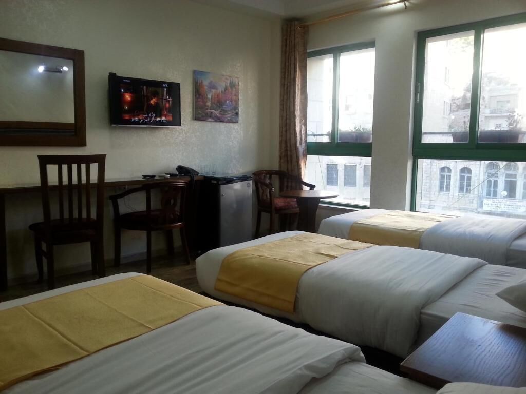 Quarto de hotel com duas camas, uma escrivaninha, uma cadeira, uma TV e janela com vista para prédios.