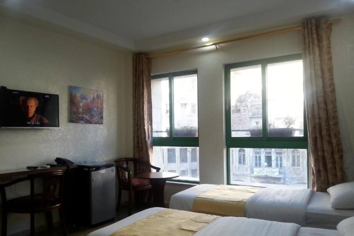 Ett hotellrum med två sängar, ett skrivbord, en stol, en tv och stora fönster med gardiner.