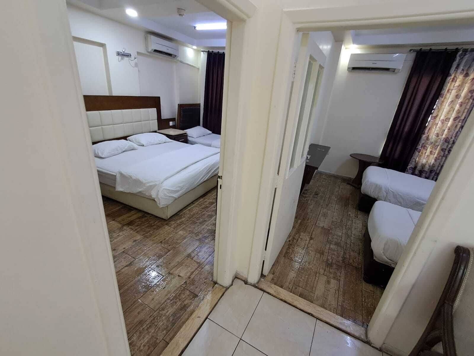 A hotel room with a bed, a sofa, an air conditioning unit, and a wooden floor.