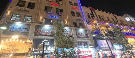 A multi-story building with illuminated signs for a hotel and various shops.