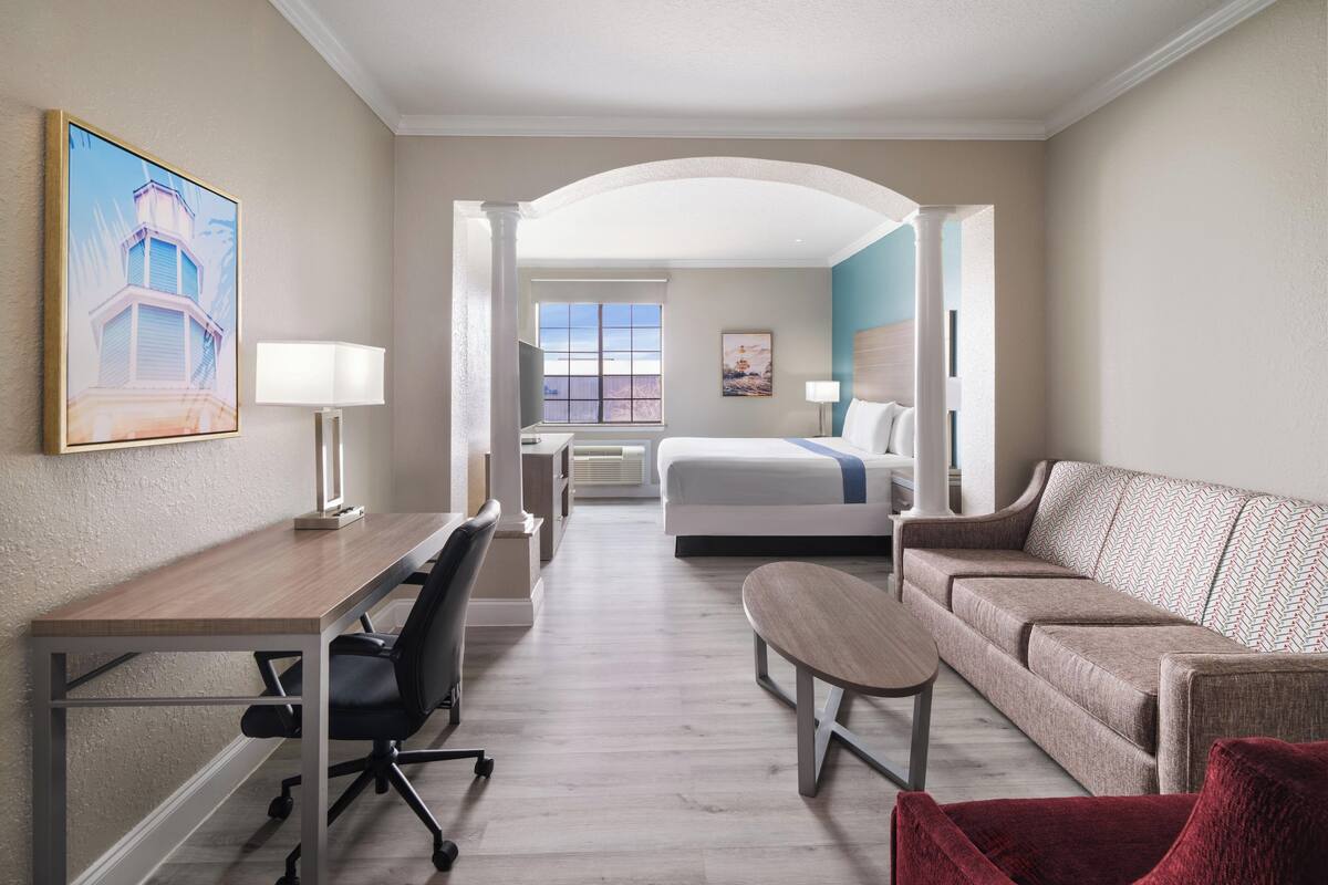 A hotel room with a desk, office chair, sofa, and a bed.