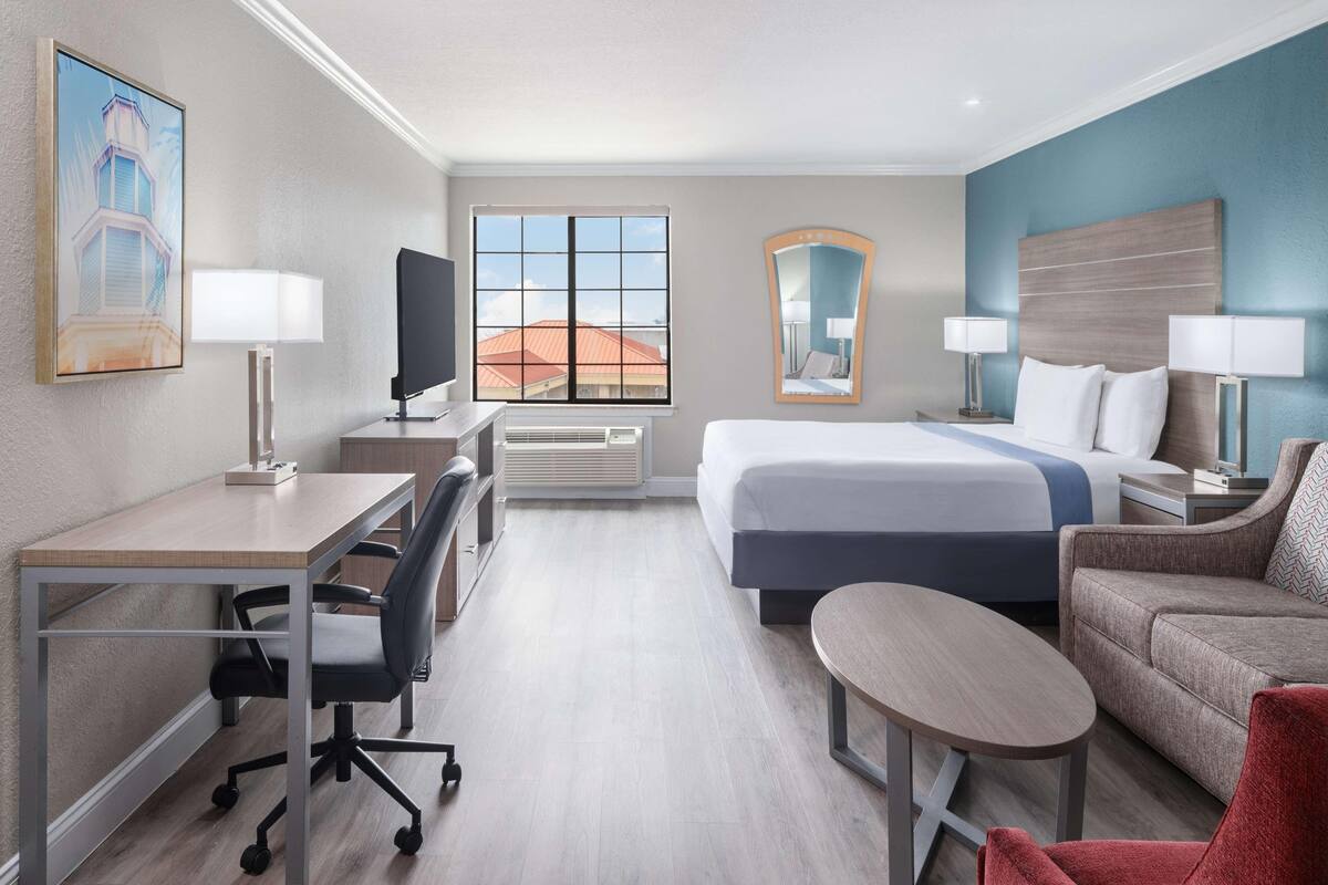 A hotel room with a bed, desk, chair, and a small table.