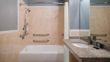 A modern bathroom with a bathtub, a shower with grab bars, a granite countertop sink, and a large mirror.