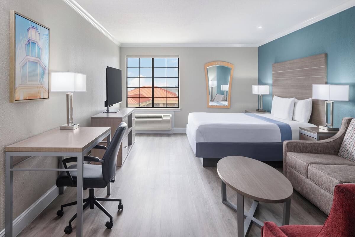 A hotel room with a bed, desk, chair, and a small table.