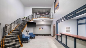 A spacious lobby with a curved staircase, a reception desk, and a seating area with blue chairs. - Melrose @ Seabrook, BW Signature Collection (Seabrook)
