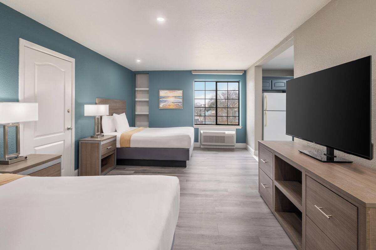 A hotel room with two beds, a TV, a desk with a lamp, a window with a view, and a painting on the wall.
