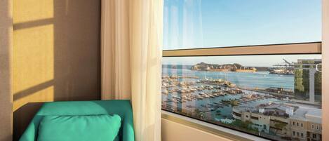 Ein Zimmer mit Blick auf eine Marina und Boote, ein Türkis-Sessel und ein Fenster mit durchsichtigen Vorhängen.