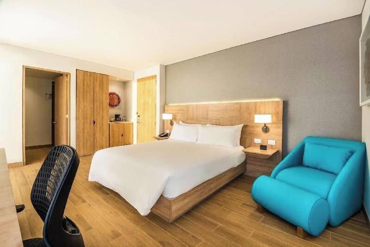 A hotel room with a bed, a chair, a desk, and a wardrobe.