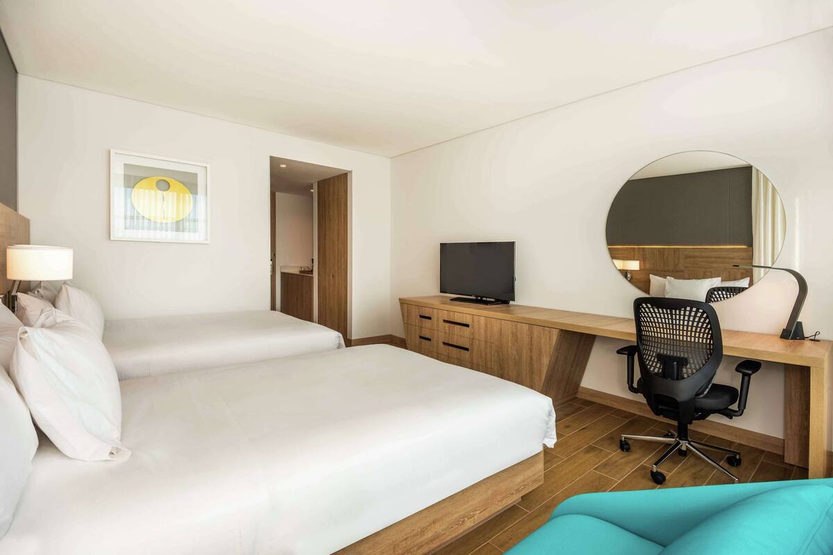 A hotel room with two beds, a desk with a computer, a TV, and a mirror.