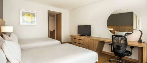 A hotel room with two beds, a desk with a computer, a TV, and a mirror.