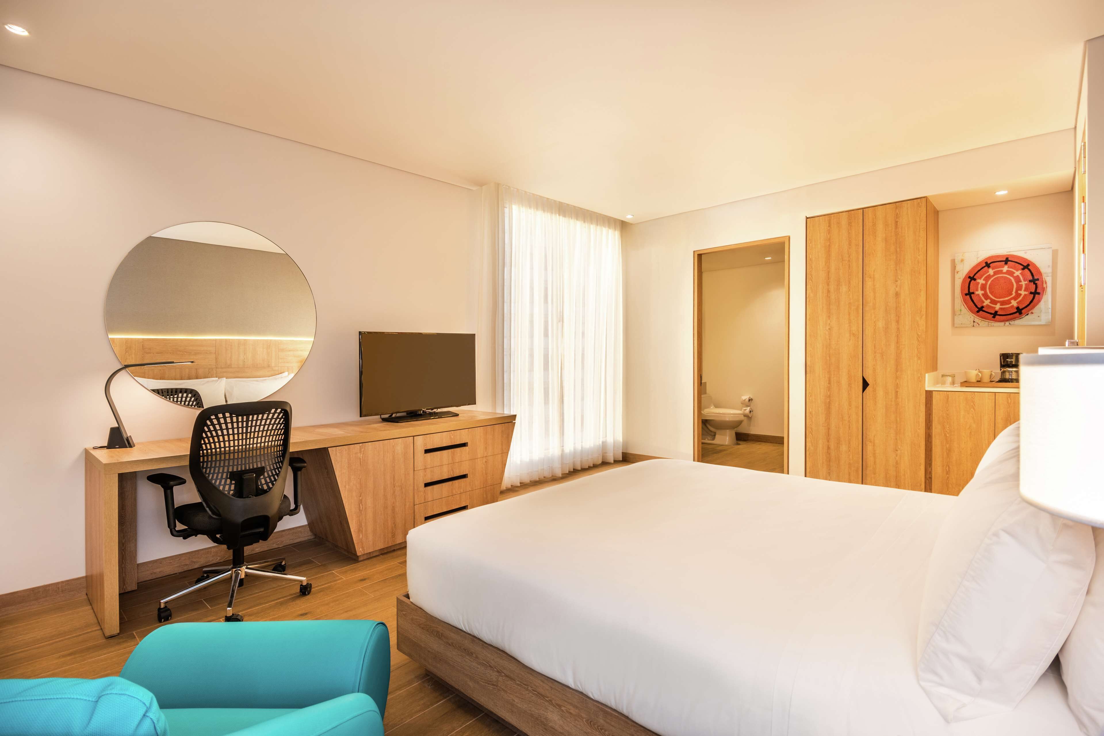 A modern hotel room with a large bed, a desk with a chair, a television, and a wardrobe.