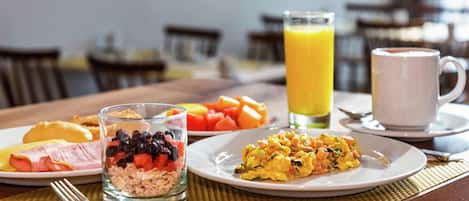 Un desayuno con platos de comida, un vaso de zumo de naranja y una taza de café.