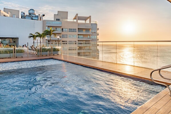 A rooftop pool with a view of the ocean at sunset, surrounded by modern buildings. - Hilton Garden Inn Santa Marta (Santa Marta)