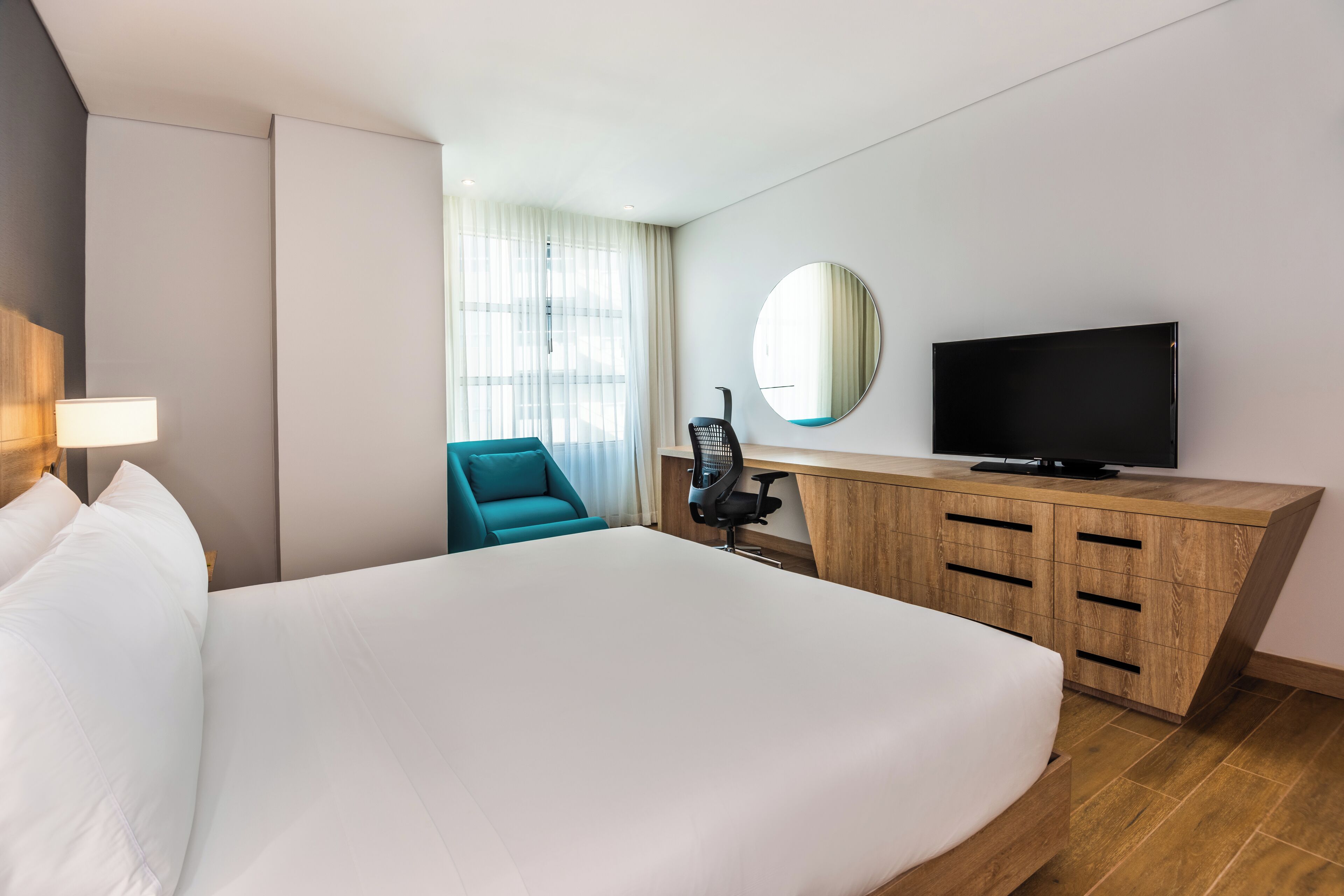 Une chambre d’hôtel avec un grand lit, un bureau avec une télévision, une chaise et une fenêtre avec des rideaux.