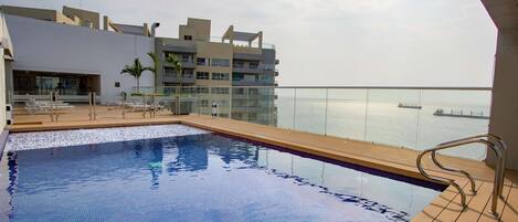 A pool area with a view of the sea and a modern building in the background.
