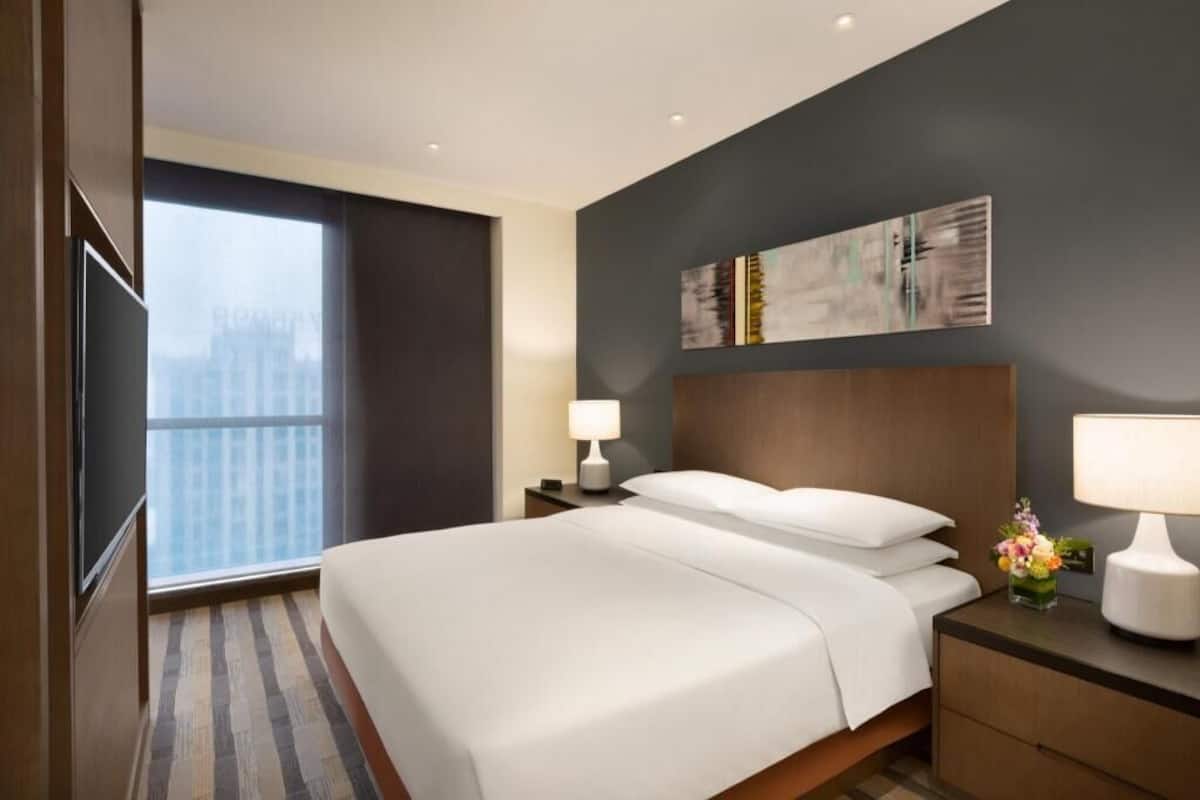 Hotelkamer met een groot bed, nachtkastje met een lamp, een kunstwerk aan de muur en een raam met uitzicht over de stad.