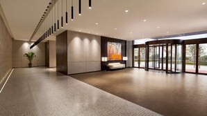 Een ruime lobby met een modern design, met een grote zithoek, een potplant en een groot kunstwerk aan de wand.