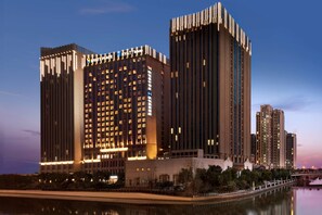 Un hôtel de grande hauteur, avec de nombreux étages, un plan d’eau aux reflets scintillants devant et un ciel dégagé.