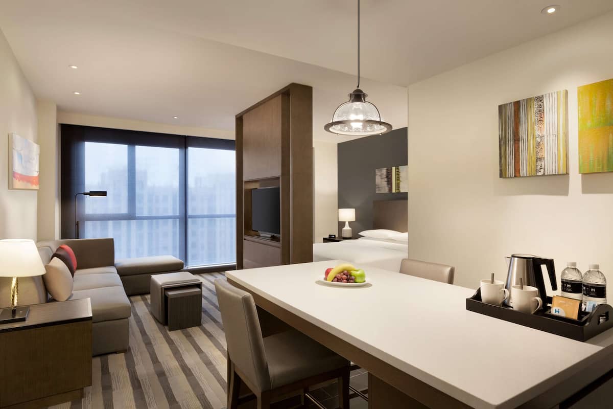 Een moderne hotelkamer met een eethoek, een bank, een bijzettafeltje en een groot raam met uitzicht op de stad.