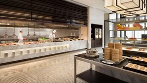 Een moderne buffetopstelling met een kok die eten bereidt, een marmeren aanrecht en diverse gerechten die op de achtergrond worden gepresenteerd.