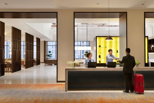 Un hall d’hôtel moderne avec un comptoir d’accueil, un espace salon et de grandes fenêtres.