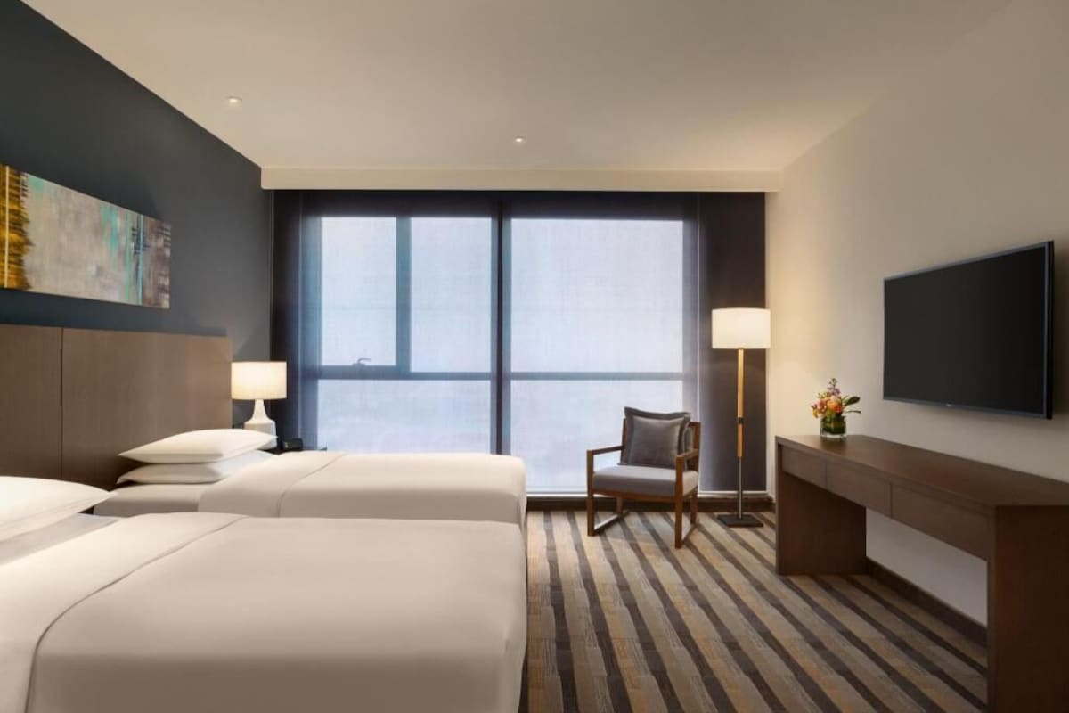 Une chambre d’hôtel avec deux lits, un bureau, une chaise, une télévision et une grande fenêtre.