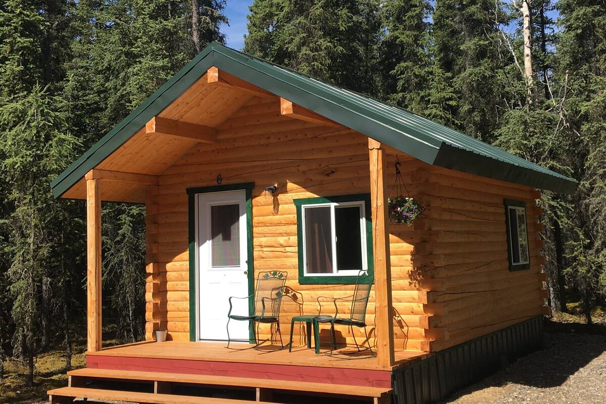 A wooden cabin with a porch, two windows, and a door.