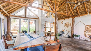 A spacious dining area with a long wooden table, chairs, and a thatched roof ceiling. - Socialtel Maderas (San Juan del Sur)
