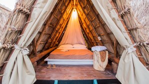 A cozy, thatched-roof tent with a bed, pillows, and a small wooden stool. - Socialtel Maderas (San Juan del Sur)