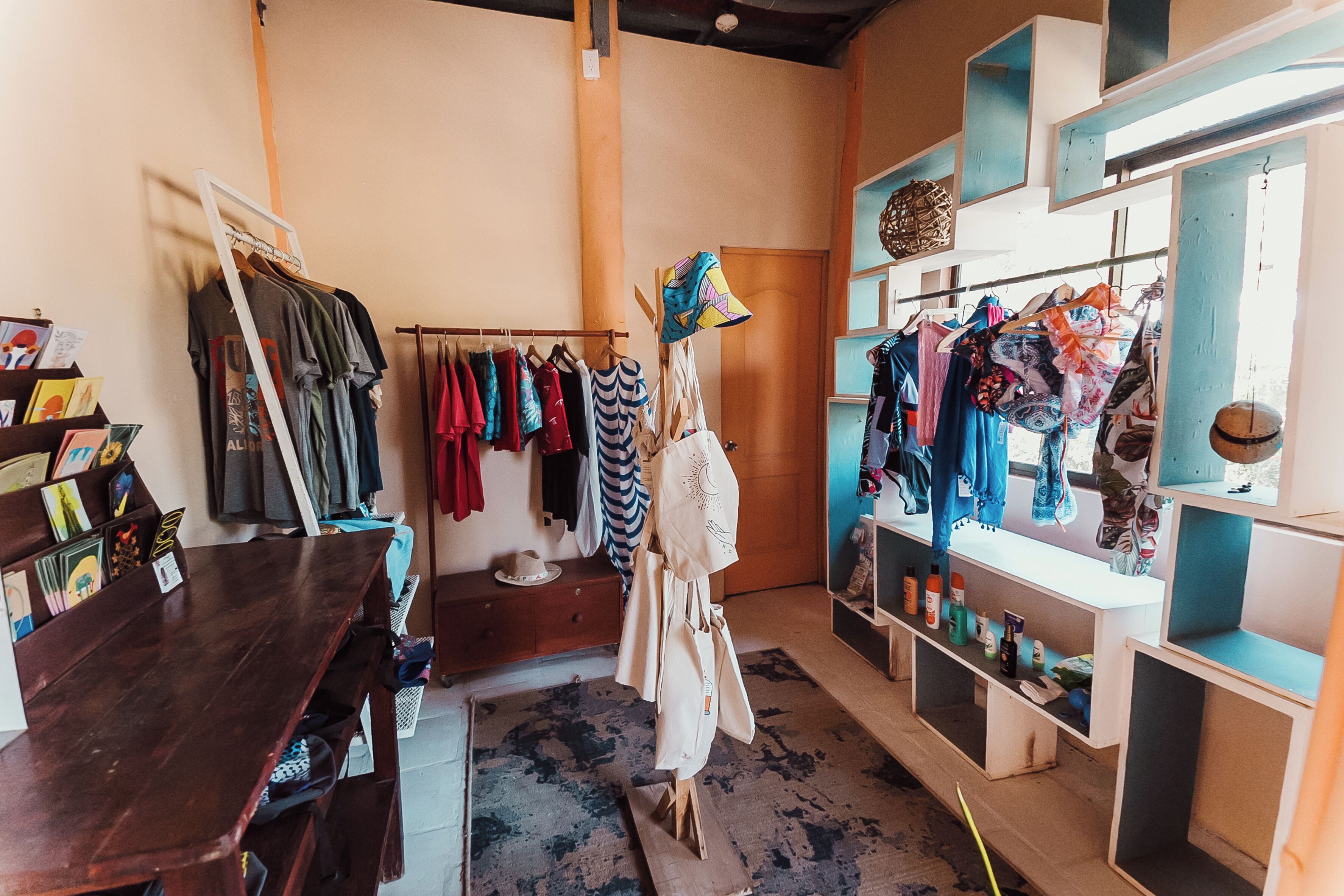 Une boutique de vêtements avec des portants remplis de vêtements, une table en bois et des étagères où sont exposés divers articles.