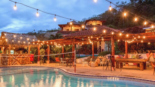 A pool area with string lights, outdoor seating, and a building with a tiled roof. - Socialtel Maderas (San Juan del Sur)