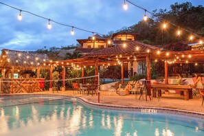 A pool area with string lights, outdoor seating, and a building with a tiled roof. - Socialtel Maderas (San Juan del Sur)